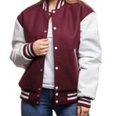 A woman wearing a maroon and white varsity jacket with leather sleeves and wool body, buttoned up with metal buttons.